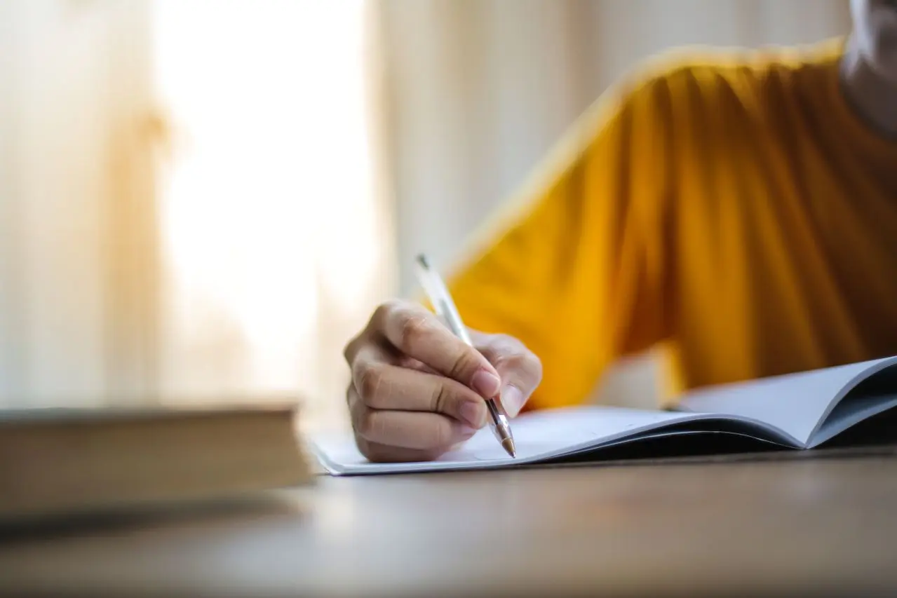 pexels-olly-3807741 Person writing in a notebook in soft natural light.